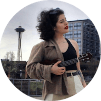 a woman holding a ukule in front of the seattle skyline